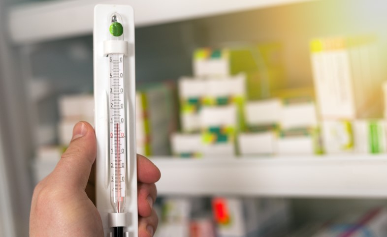 Thermometer held in front of pharmacy fridge